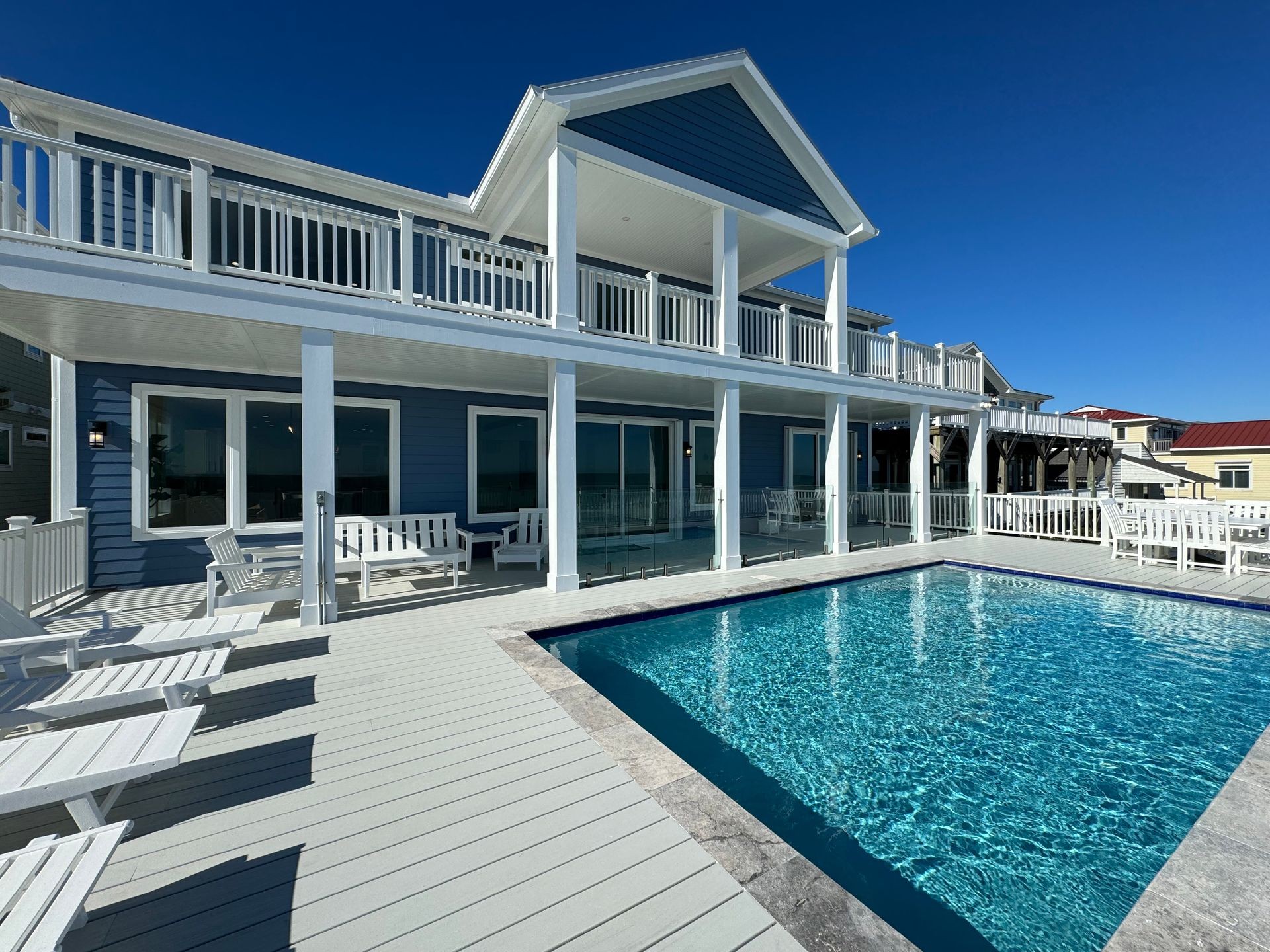 Modern two-story house with a balcony and deck surrounding an outdoor pool under a clear blue sky.